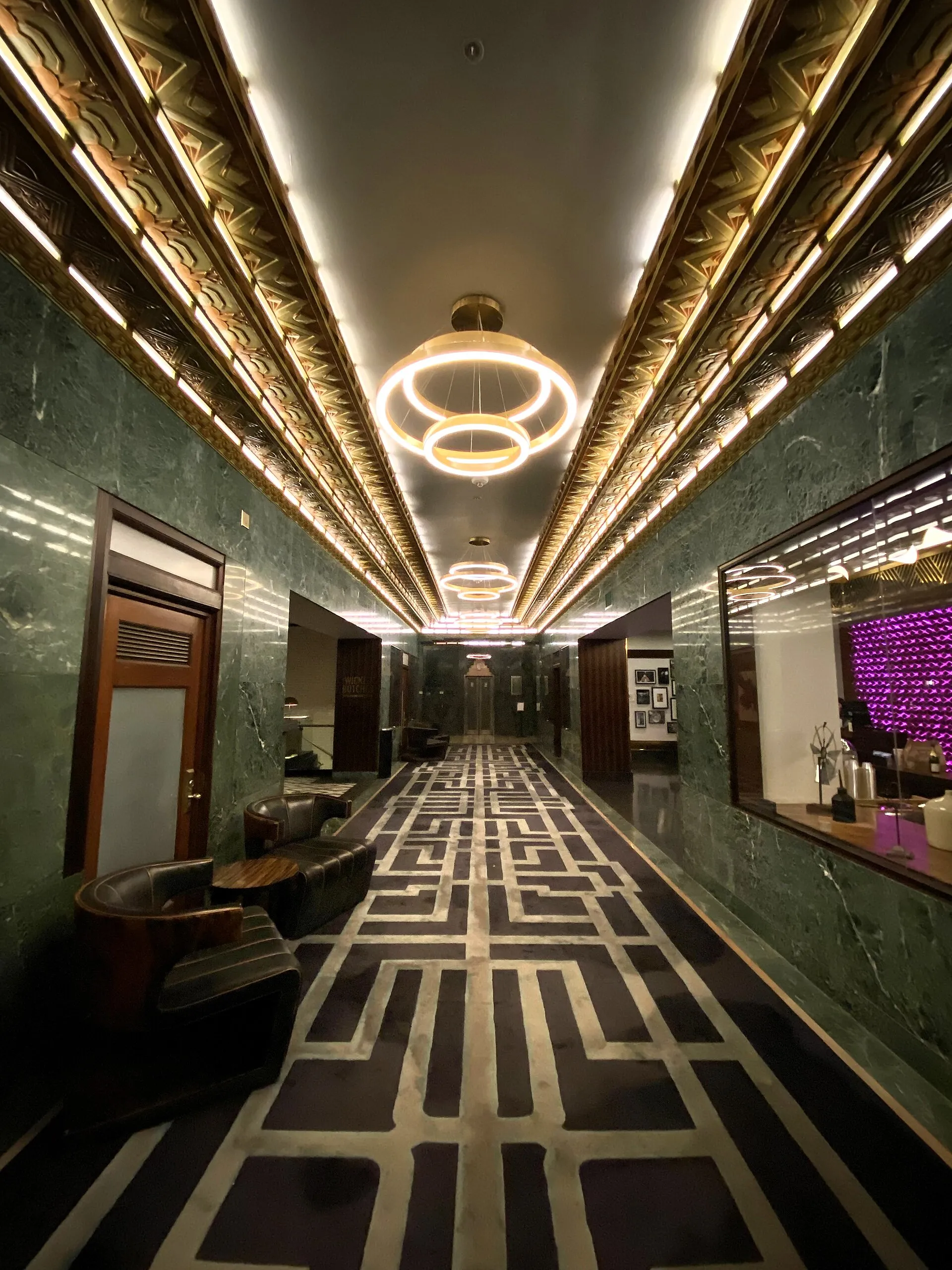 A long hotel lobby with glowing ceiling coves and ring pendants