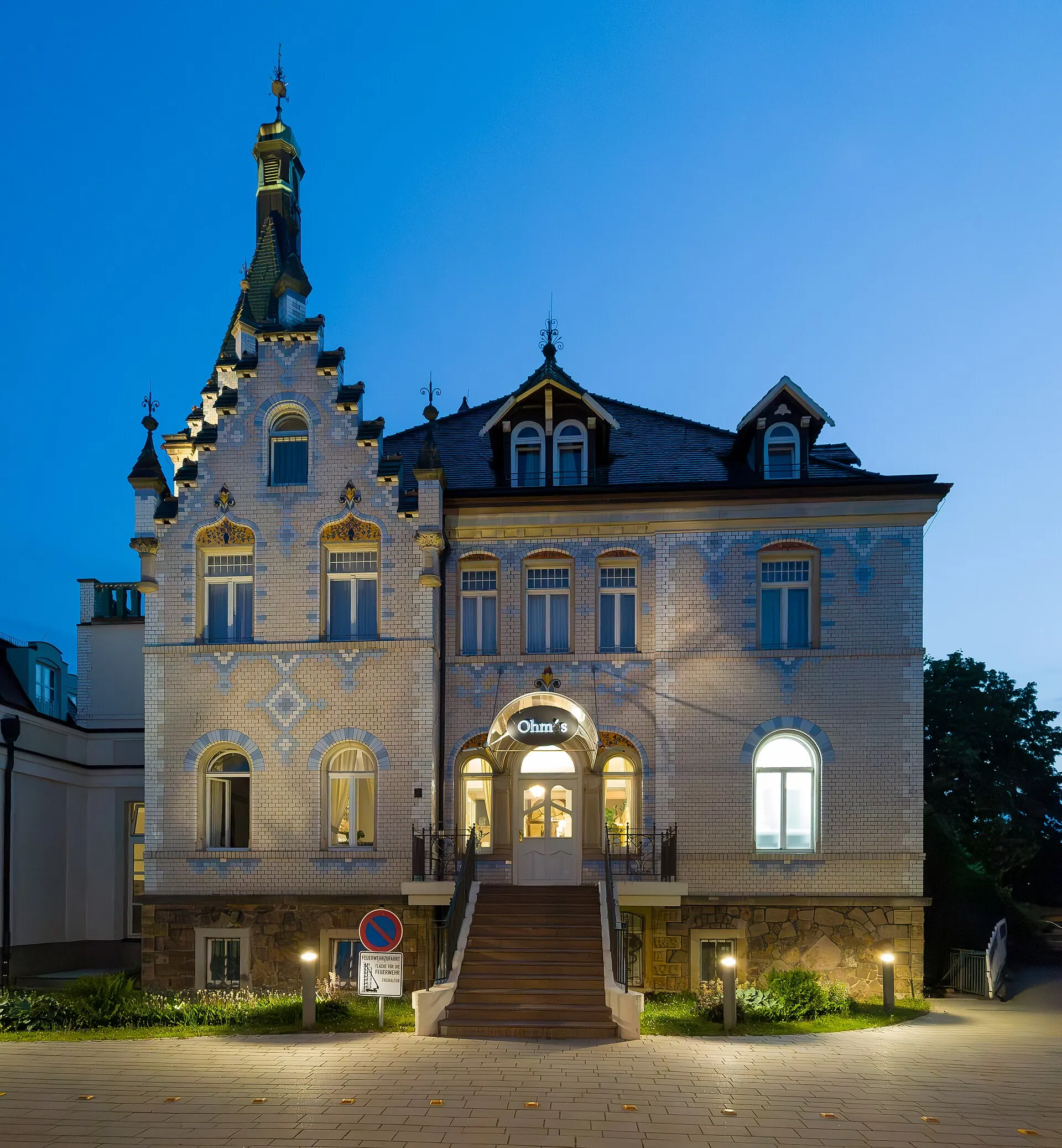 A brick villa at dusk with lit windows and garden bollards