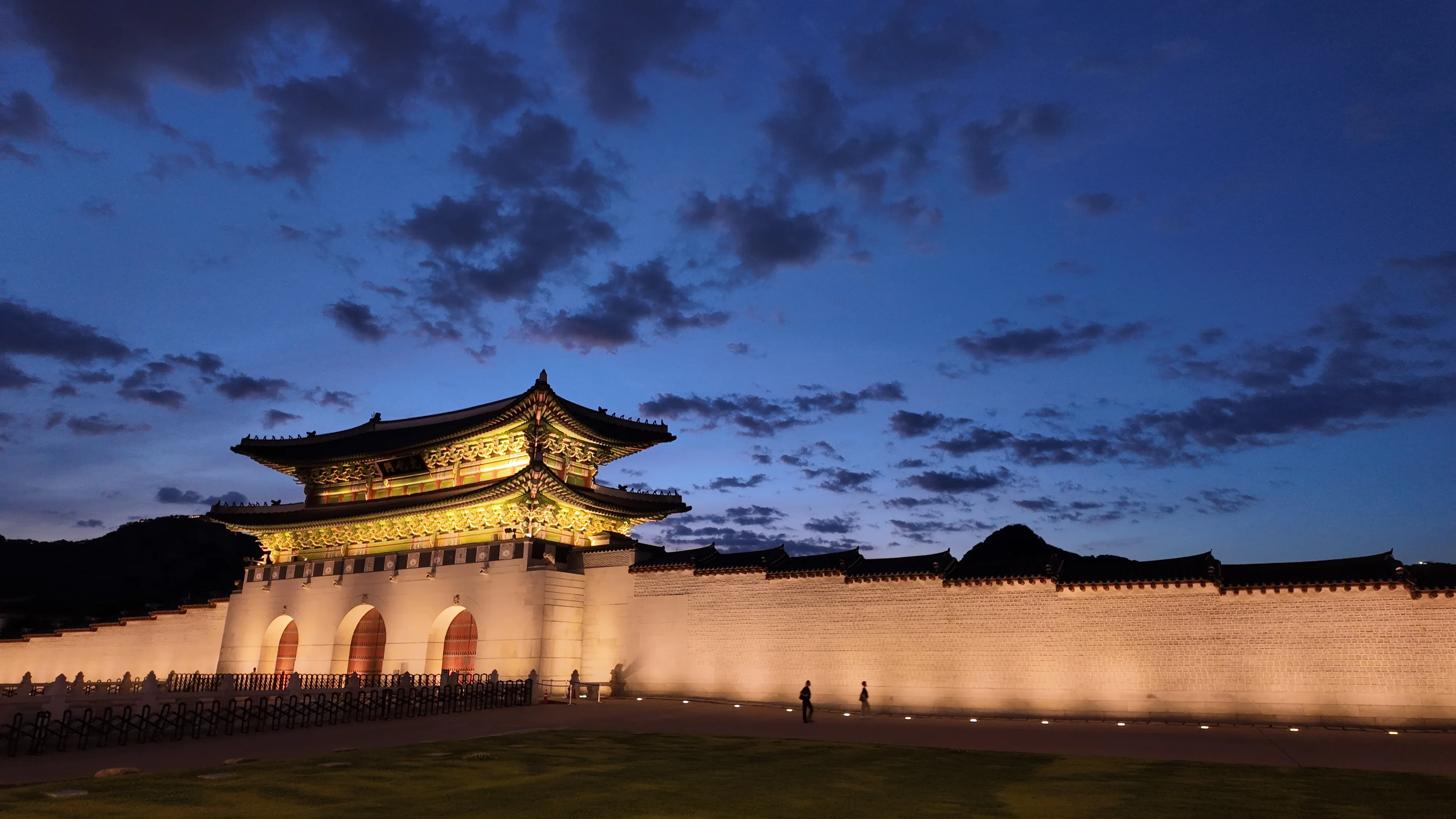 A long palace wall and gate washed in warm light under a deep blue evening sky